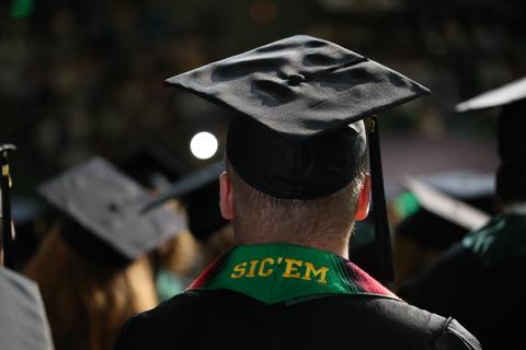 Graduating Student in camp and gown with Sic'em embroidered on sash